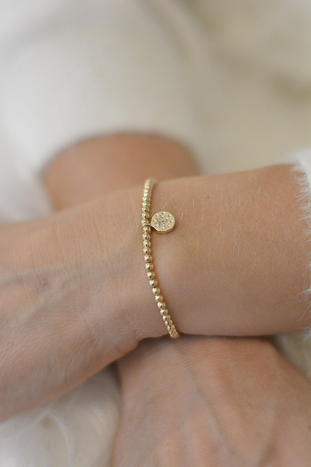Ein getragenes Armband am Handgelenk in gold und mit einem funkelnden Anhänger. Man sieht die Handgelenke vor weißem Hintergrund 