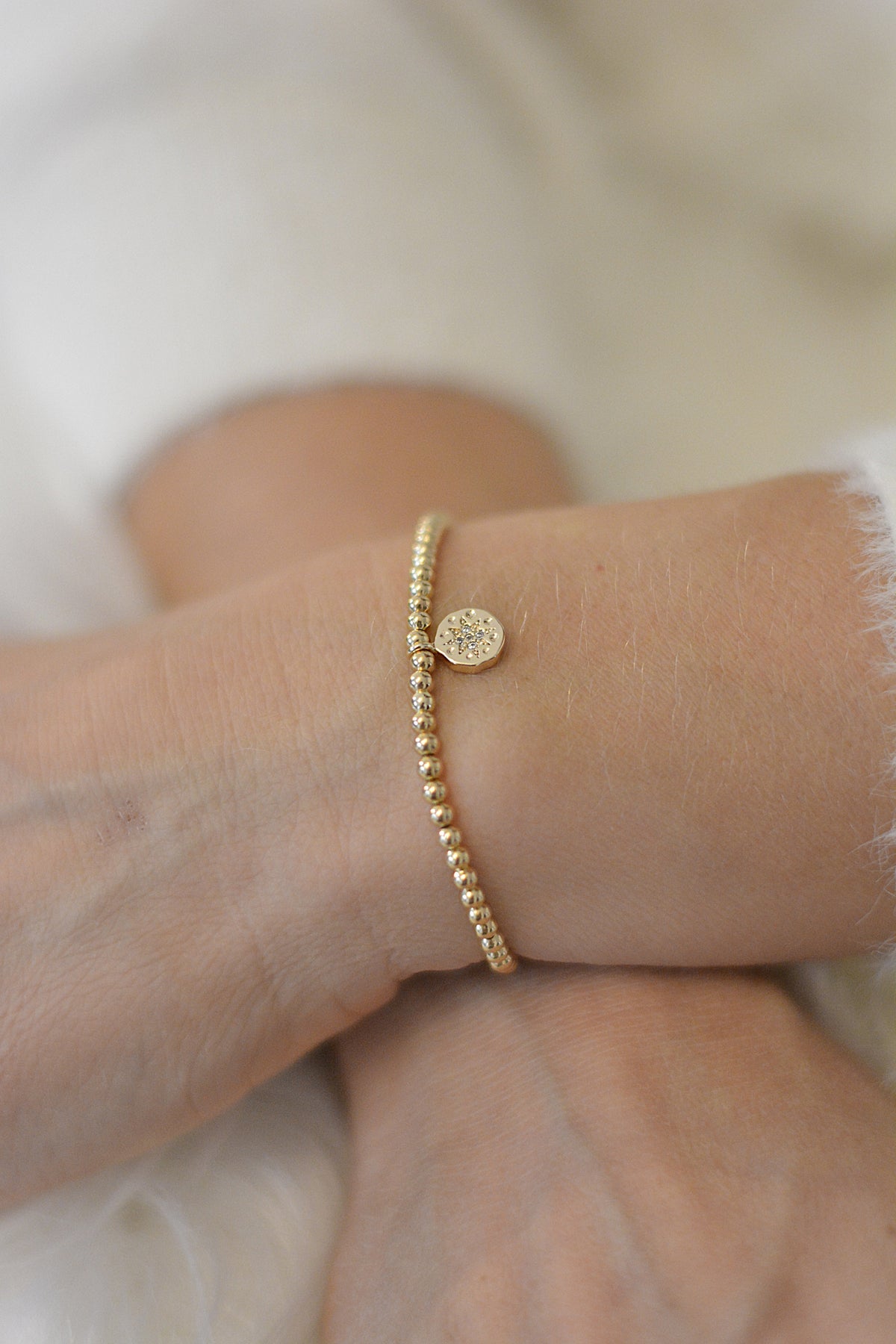 Ein getragenes Armband am Handgelenk in gold und mit einem funkelnden Anhänger. Man sieht die Handgelenke vor weißem Hintergrund 