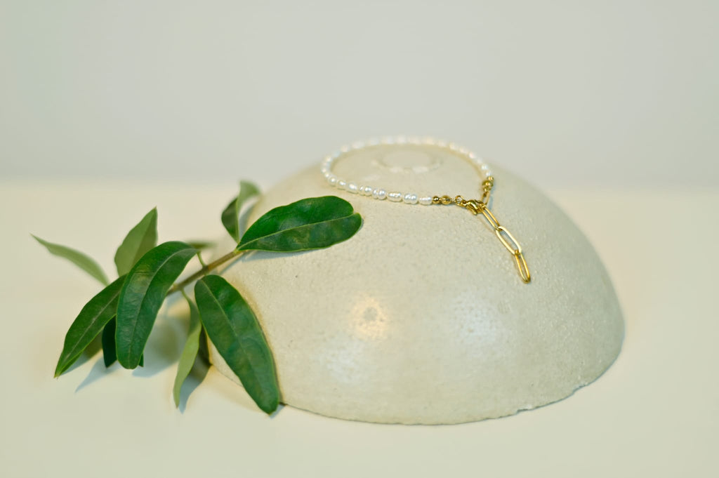 Klassische Süßwasserperlen Armkette mit goldenen Verschluss. Das Armband liegt auf einem Stein und im Hintergrund ist ein Olivenzweig